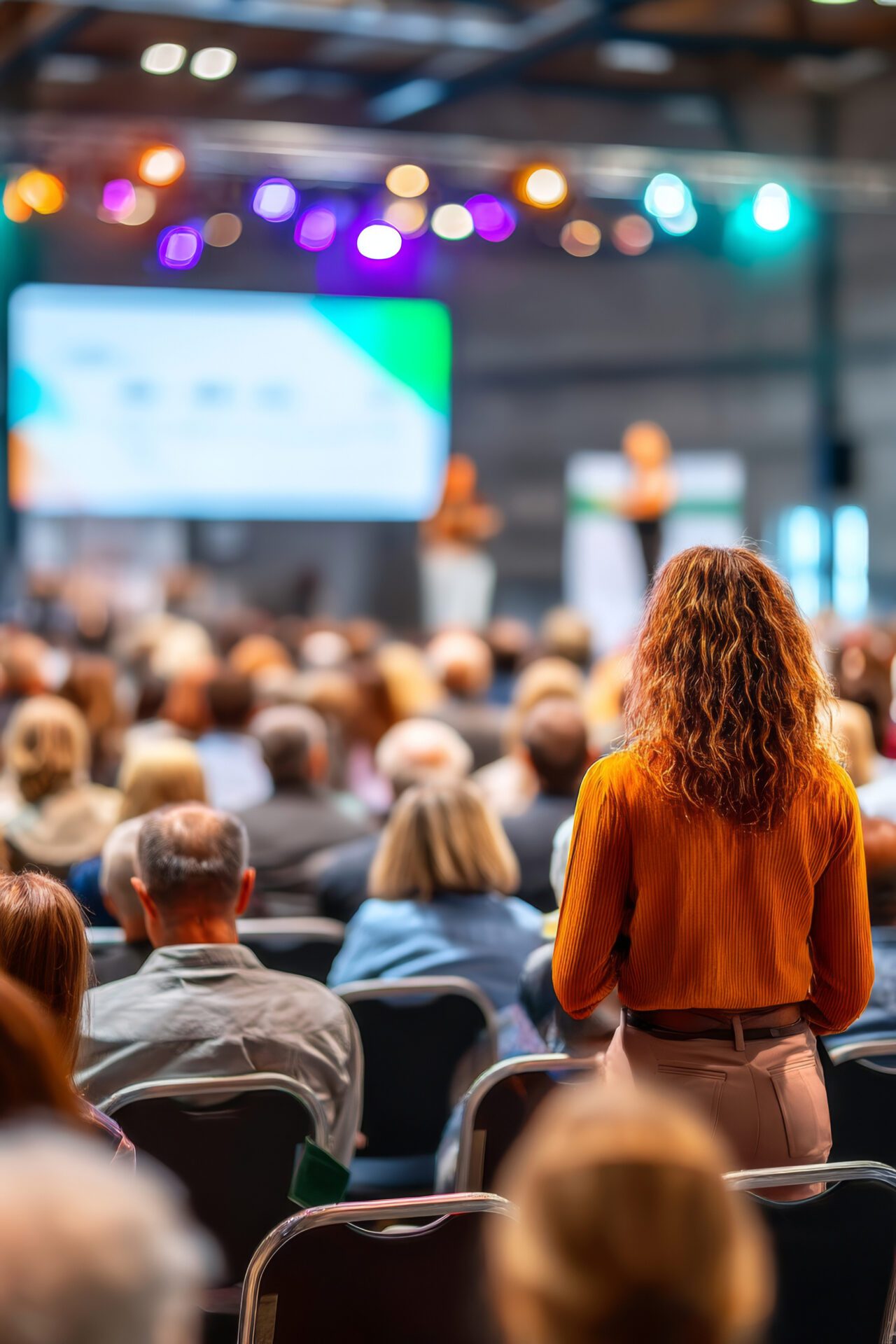 Woman standing among audience during interactive conference session with speaker on stage